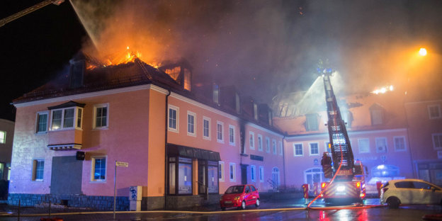 Ein Haus steht bei Nacht in Flammen. Die Feuerwehr versucht zu löschen.