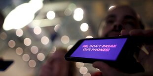 Ein Mann hält ein iPhone in die Kamera. Auf dem Display steht: „FBI don´t break our Phones".