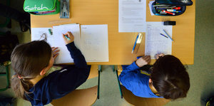 Ein Schüler und eine Schülerin sitzen an einem Tisch und arbeiten. Das Bild zeigt sie von oben.