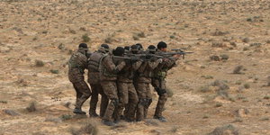 Soldaten stehen während einer Übing zusammengedrängt in der Steppe und visieren mit ihren Gewehren ein Ziel an.