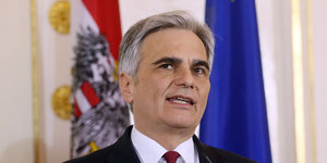Mann im Anzug mit dunkelroter Krawatte vor Österreich und EU-Flaggen