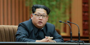 Nordkoreas Machthaber Kim Jong Un sitzt an einem Tisch. Darauf stehen Mikrofone.