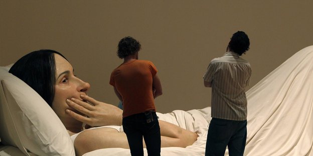 zwei Männer betrachten das riesige Foto einer Frau, die im Bett liegt