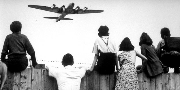Kinder an einem Holzzaun schauen zu einem Flugzeug hoch. Schwarz-Weiß-Aufnahme