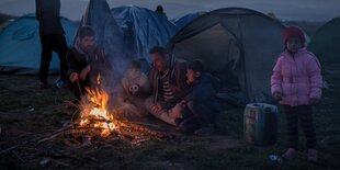 Menschen sitzen und stehen vor einem Zelt