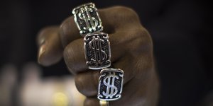 Eine Hand mit drei Ringen an den Fingern, die das Dollar-Symbol ziert.