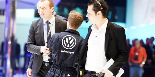 Männer halten einen anderen Mann in VW-Anzug am Arm fest.