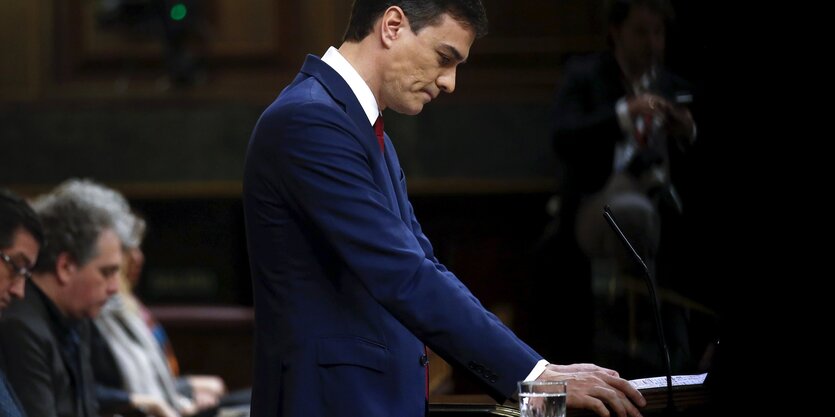 Pedro Sánchez steht an einem Rednerpult und schaut zu Boden