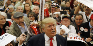 Donald Trump macht ein ärgerliches Gesicht, hinter ihm drängen sich die Leute, um ein Autogramm zu bekommen.