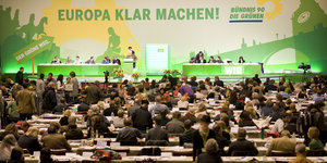 Menschen sitzen an Tischen, dahinter Bühne mit großem Transparent, auf dem steht "Europa klarmachen - Bündnis 90 / Die Grünen"