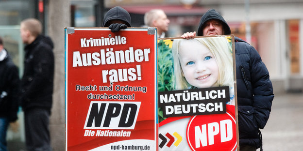 Zwei Männer halten Schilder mit den Aufschreiften Kriminelle Ausländer Raus und Natürlich Deutsch - NPD