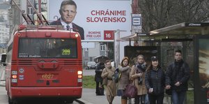 Menschen, ein Bus und ein Wahlkampfplakat