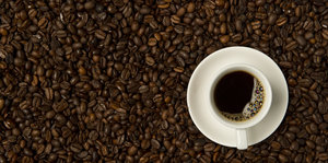 EIne Tasse Kaffee steht auf viele Kaffeebohnen