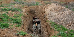 Ein syrischer Kämpfer schalft mit seinem Gefahr in einem Erdloch.