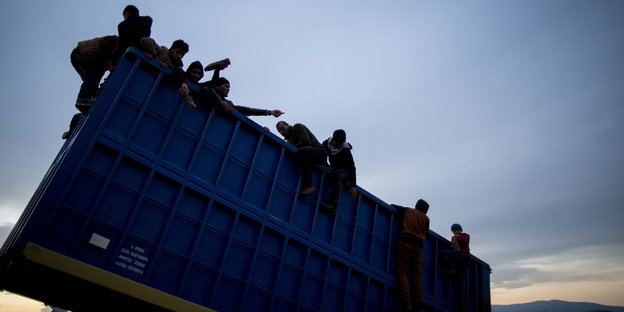 Neun Flüchtlinge klettern über den Rand eines Containers