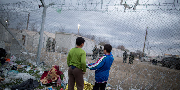 Zwei Jugentliche stehen vor einem Zaun mit Nato-Stacheldraht.
