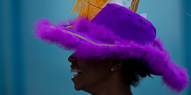 Eine lachende Frau trägt einen violetten Hut mit orangefarbenen Federn.