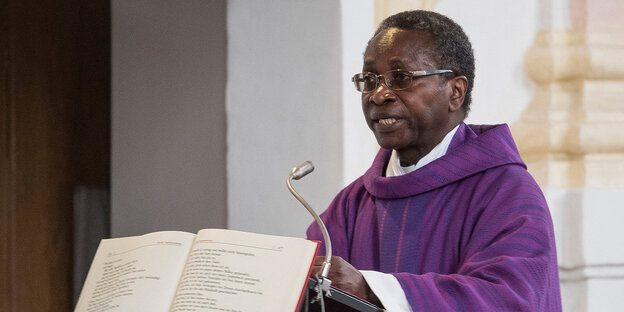 Der schwarze Pfarrer Olivier Ndjimbi-Tshiende steht am Rednerpult in einer Kirche.