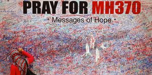 Eine Frau mit Kopfstuch schreibt etwas an eine vollgeschriebene Wand, die mit "Pray for MH370. Messages of Hope" überschrieben ist
