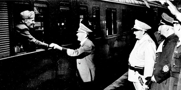Mussolini streckt seine Hand aus einem Zugfenster, Hitler hält sie, Ribbentrop und Göring stehen daneben und sehen zu.