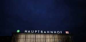 „Hauptbahnhof“ steht erleuchtet auf einem Dach. Es ist dunkel.