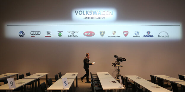 Ein Mann läuft unter einem VW-Logo in einem Konferenzraum entlang.