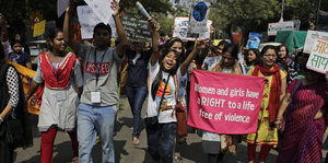 Menschen, vorwiegend Frauen, laufen auf einer Straße und halten Plakate und Schilder in den Händen