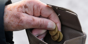 Eine mit Altersflecken bedeckte Hand greift in eine Geldbörse.