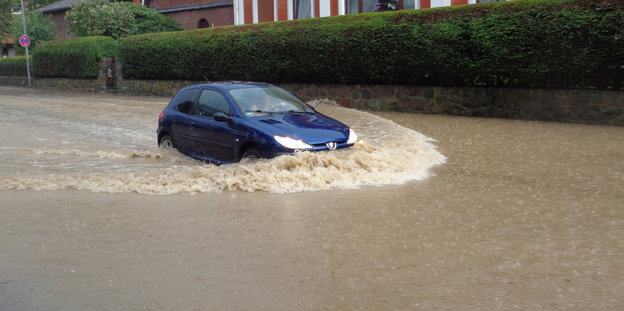Ein Auto fährt durch eine überflutetet Straße