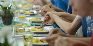 Schulkinder sitzen an einem langen Tisch und essen.