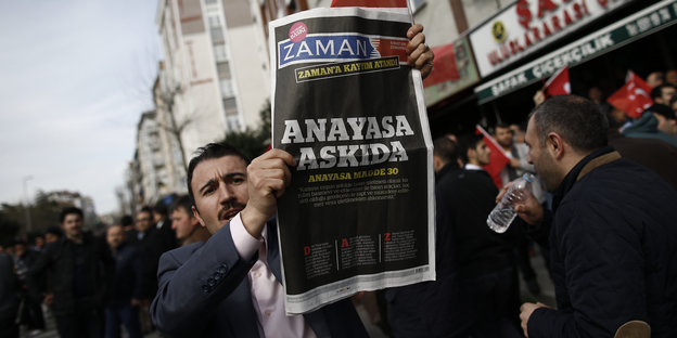 Ein Mann auf einer Demo hält eine Zeitung in die Höhe.