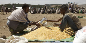 Von einem kleinen Berg mit Korn werden Hilfpäckchen abgefüllt.eferungen Lebensmittelverteilung