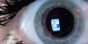 Ein Display mit einem Facebook-Likebutton spiegelt sich in der Pupille eines Auges mit geschminkten Wimpern