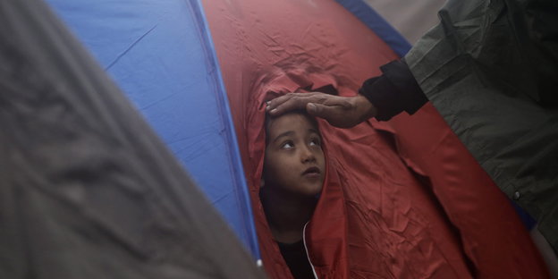 Ein Kind schaut aus einem Zelt, eine Hand streichelt über seinen Kopf