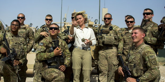 eine Frau in weißer Bluse zeigt inmitten von Soldaten in Uniform auf etwas vor ihr