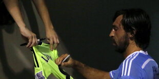 Andrea Pirlo schreibt ein Autogramm auf ein Trikot.