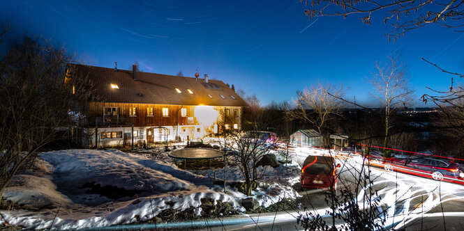 Der Bauernhof bei Nacht. Die Leuchtspuren der Autos erhellen die sonst einsamen Straßen