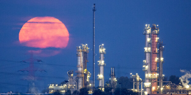 Ein roter Mond geht hinter einer Erdölraffinerie im Hamburger Hafen unter.