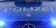 Der Schriftzug "Polizei" ist auf einem Polizeifahrzeug mit Blaulicht zu sehen.