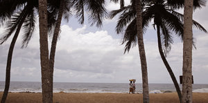 Zwei Menschen laufen an einem Strand mit Palmen