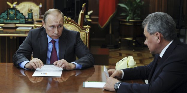 Wladimir Putin und Sergey Shoygu sitzen an einem Tisch und reden.