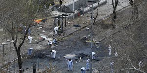 Menschen in weißen Anzügen arbeiten auf einer von einer Bombe zerstörten Straße.