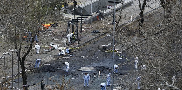 Menschen in weißen Anzügen arbeiten auf einer von einer Bombe zerstörten Straße.