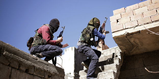 Zwei maskierte Kämpfer mit Gewehren auf einem Häuserdach