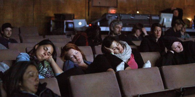 Menschen sitzen schlafend in einem Theaterraum.
