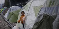 Ein Kind in einem orangenen Anorak schaut aus einem Zelt