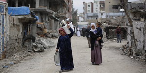 Zwei Frauen tragen Gepäck und ein Kind durch eine zerstörte Straße in Cizre