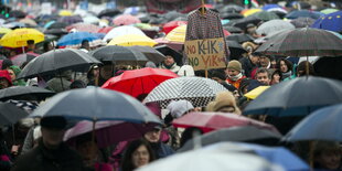 Menschen unter Regenschirmen, ein Karohemd wird hochgehalten