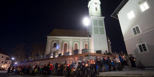 Menschen stehen im Kreis um eine Kirche und halten Kerzen