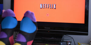 Zwei hochgelegte Füße mit bunten Socken vor Fernsehgerät, auf dem "Netflix" steht